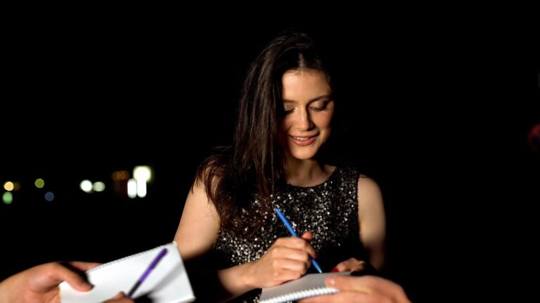Woman signing autographs in fans notebooks at evening party